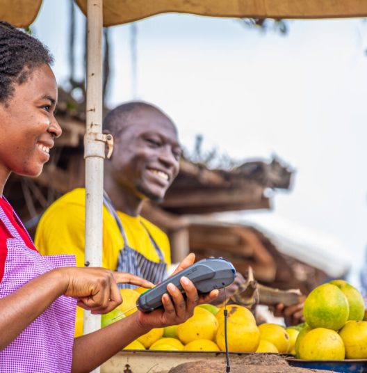 african woman using a pos machine in a market smiling, other people in the background trading